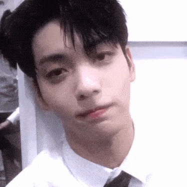 a young man in a white shirt and tie is taking a selfie with his phone .
