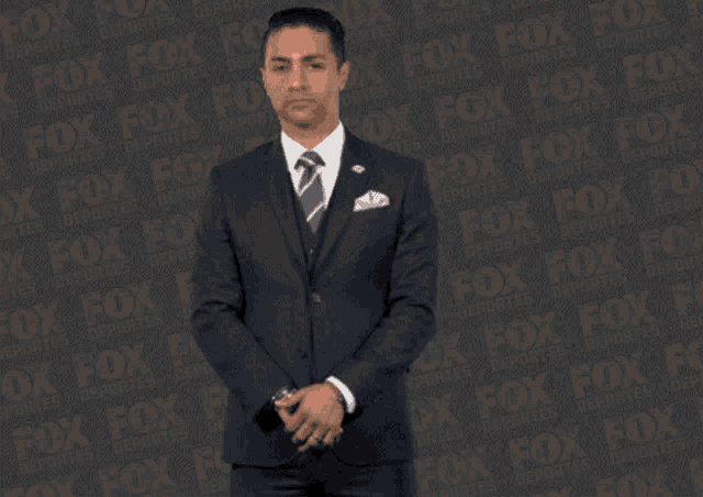 a man in a suit and tie is standing in front of a fox deportes background