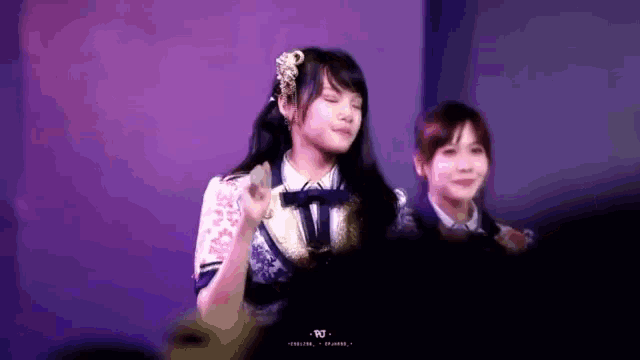 two girls are standing on a stage in front of a crowd .