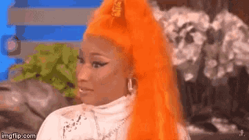 a woman with bright orange hair is sitting on a couch and making a funny face .