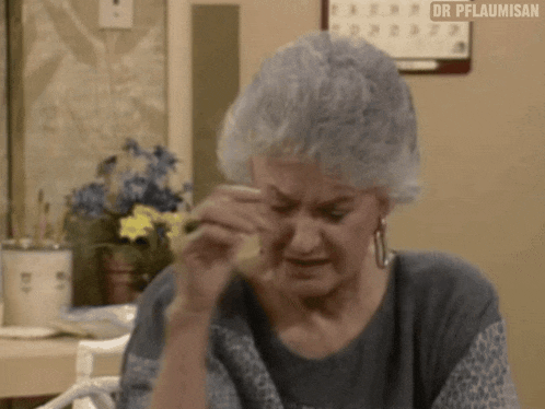 an elderly woman is crying while sitting at a table with flowers in the background .