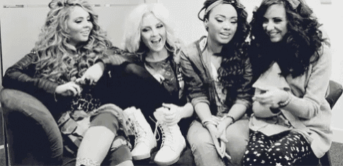 a black and white photo of four women sitting on a couch laughing .