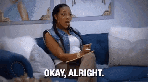 a woman is sitting on a blue couch holding a clipboard and saying `` okay , alright . ''