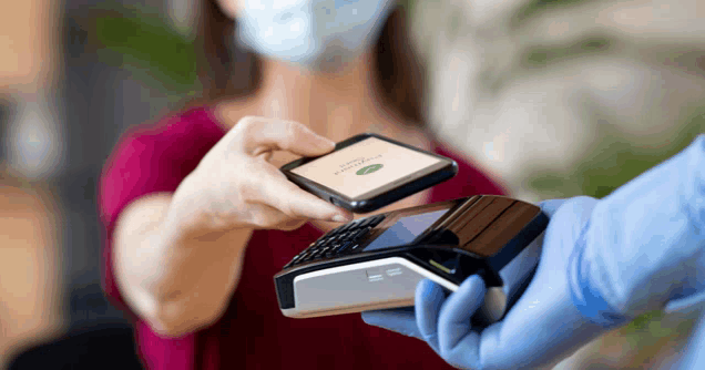 a woman wearing a mask is paying with a phone