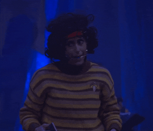 a person in a yellow and black striped sweater is standing in a dark room