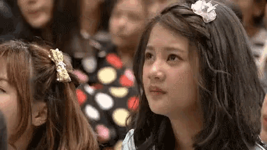 a girl with a flower in her hair is sitting in front of a crowd of people .