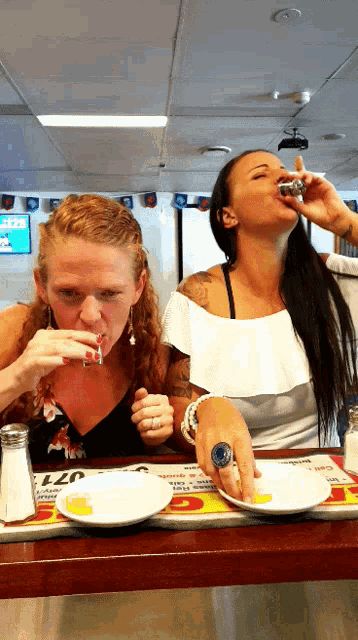 two women are sitting at a table with plates and salt and pepper shakers on it and a sign that says 077 on it