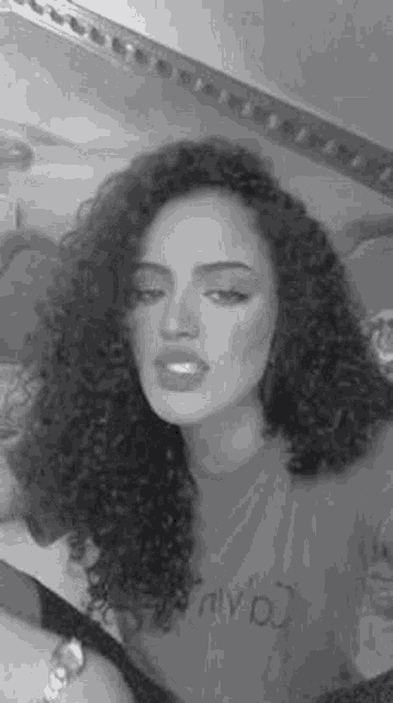 a black and white photo of a woman with curly hair and a t-shirt .