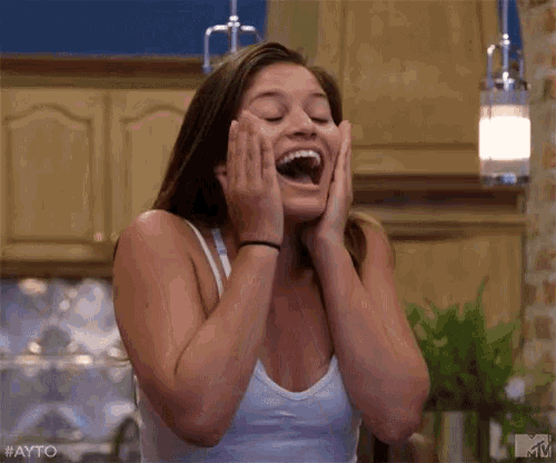 a woman is sitting at a table with her hands on her face and a surprised look on her face .