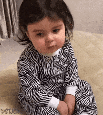 a baby wearing a zebra print pajama is sitting on a bed
