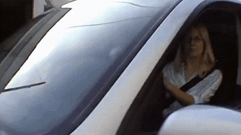 a woman is driving a white car with her head out the window