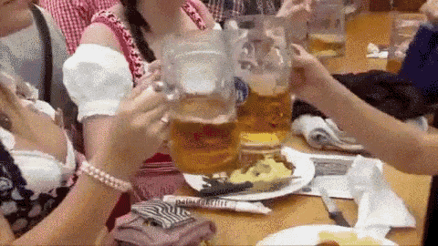 a group of people are sitting at a table drinking beer and toasting .