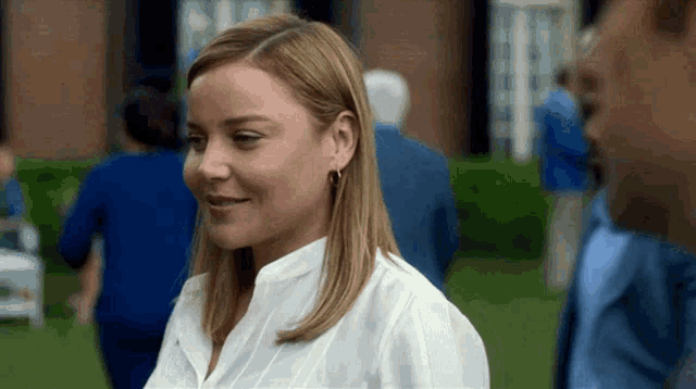 a woman in a white shirt and earrings is smiling while standing in front of a building .