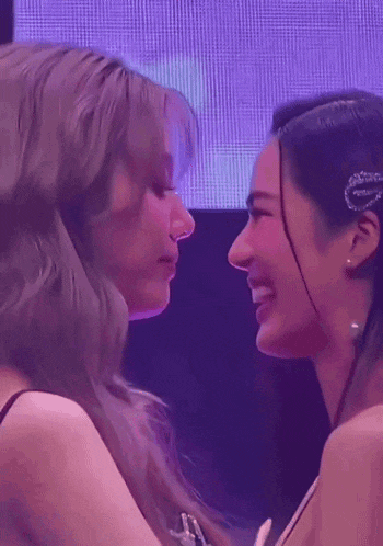 two women are kissing each other on the nose in front of a purple screen .