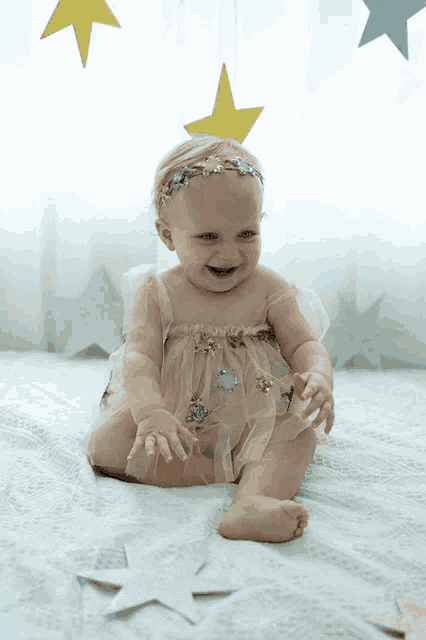 a baby wearing a headband and a dress is sitting on a bed