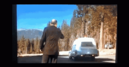 a man in a suit walks down a road with a white van in the background