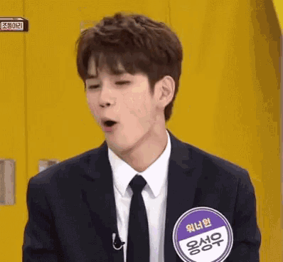 a young man in a suit and tie is making a funny face while standing in front of a yellow wall .