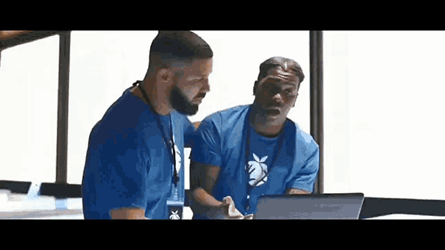 two men are standing next to each other looking at a laptop computer .