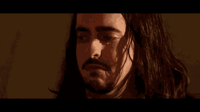 a man with long hair and a beard is crying with a tear running down his face .