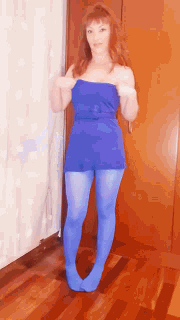 a woman in a blue dress and blue tights is standing in front of a door .