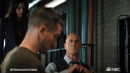 a man is adjusting his tie in a scene from organized crime on nbc