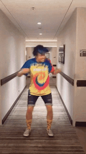 a man is dancing in a hallway wearing a tie dye shirt that says ' hawaii ' on it