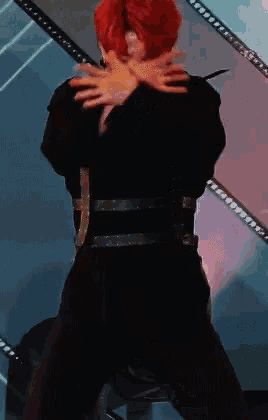 a man with red hair is dancing on a stage with his arms crossed