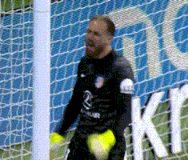 a soccer goalie is holding a ball in front of a net with the letter k on it
