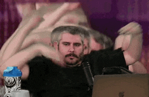 a man with a beard is sitting in front of a laptop computer making a heart shape with his hands .