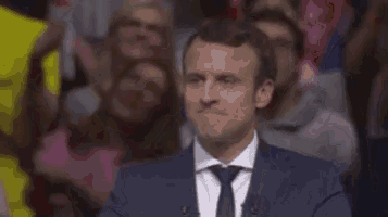 a man in a suit and tie is smiling while sitting in front of a crowd .