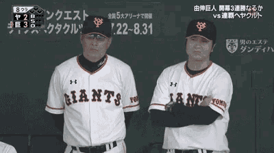 two baseball players wearing giants jerseys stand in front of a blackboard