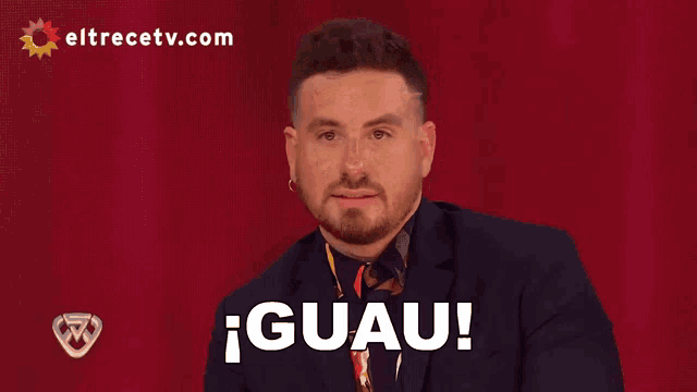 a man in a suit says guau in front of a red background