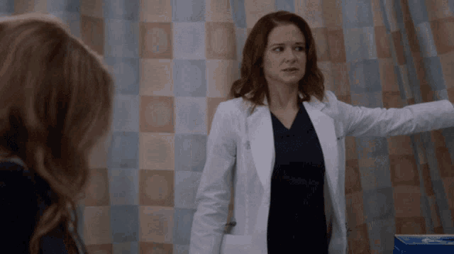 a woman in a lab coat is talking to another woman in a hospital room