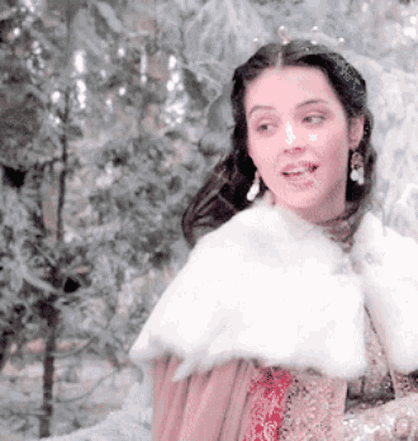 a woman wearing a fur cape and earrings stands in a snowy forest