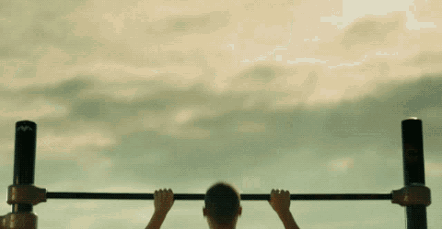 a man is doing a pull up on a bar with a cloudy sky behind him