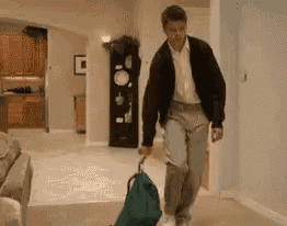 a man is walking down a hallway with a green bag