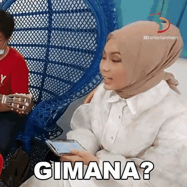 a woman wearing a hijab is holding a cell phone and says gimana ?
