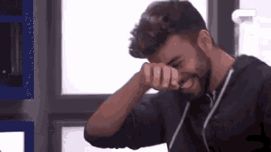 a man with a beard is covering his face with his hands .