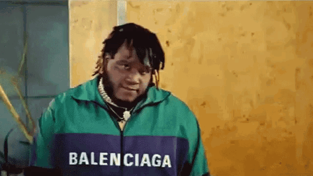 a man wearing a balenciaga jacket is standing in front of a wooden wall