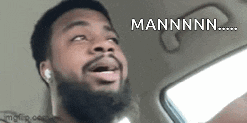 a man with a beard and ear buds is driving a car and making a funny face .