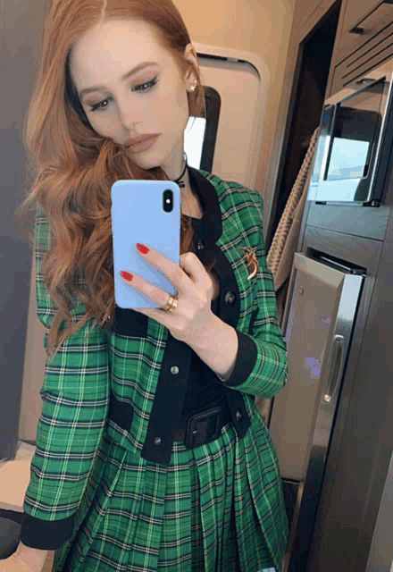 a woman in a green plaid jacket taking a selfie with her phone