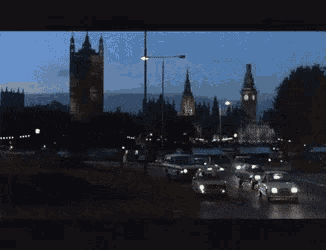 cars are driving down a street at night with a clock tower in the background