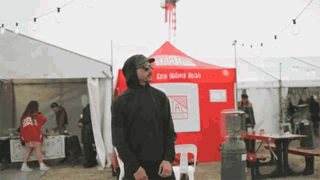 a man in a black hoodie stands in front of a tent that says good native beers
