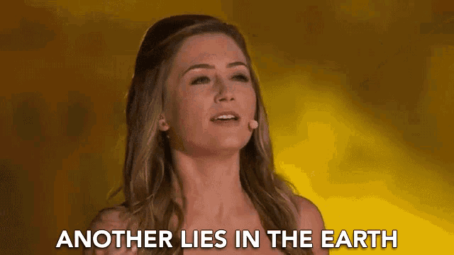 a woman is singing into a microphone with the words `` another lies in the earth '' behind her .