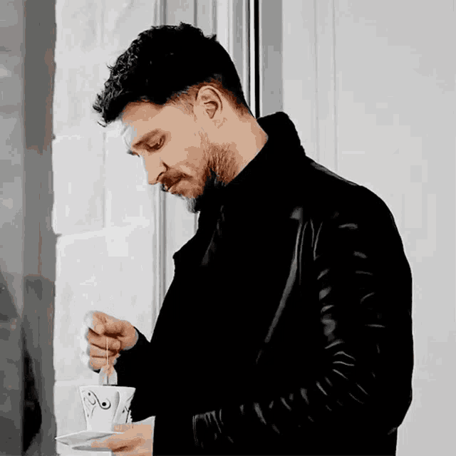 a man in a black jacket is pouring a cup of coffee