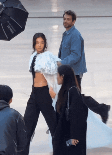 a man in a denim jacket stands next to a woman in a white crop top