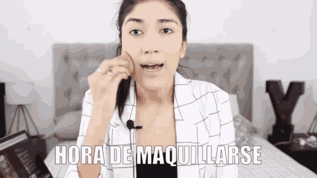 a woman is sitting on a bed with the words hora de maquillarse written above her