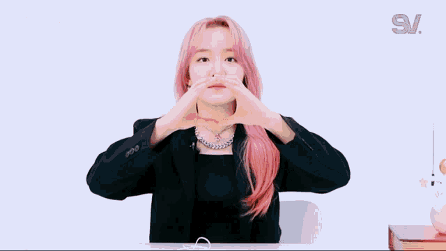 a girl with pink hair is making a heart shape with her hands