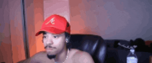 a shirtless man is wearing a red hat and sitting in a chair .