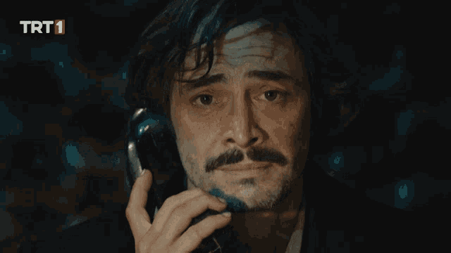 a man with a mustache is talking on a phone with trt1 on the bottom right